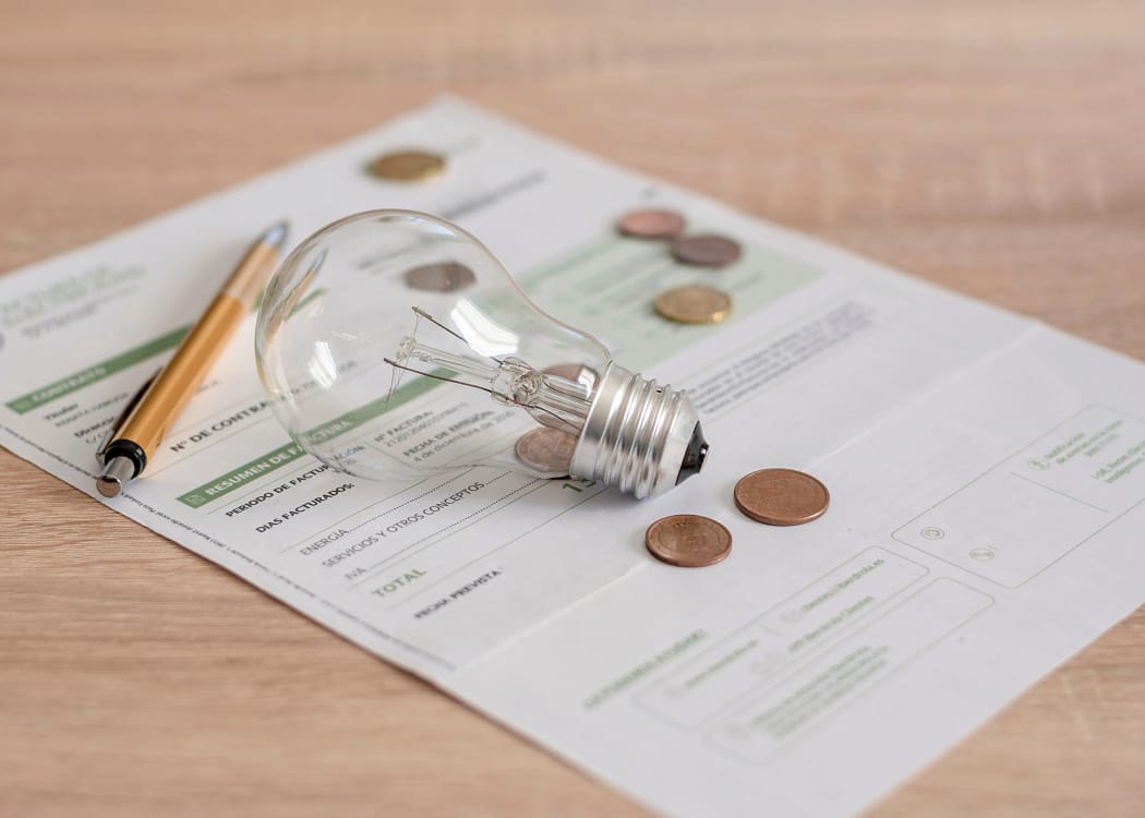 Un bec pus peste factura la energie electrică, pe care se află câteva monede și un pix
