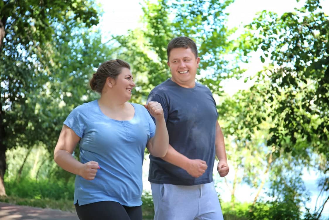două persoane plinuțe, bărbat și femeie, alergare parc, lac